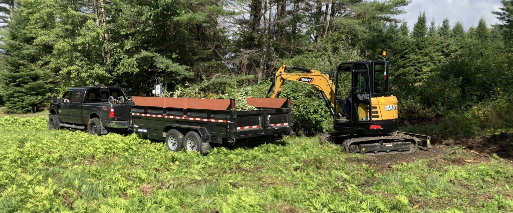 Efficient land clearing using a pickup truck, dump trailer, and mini excavator on a wooded lot - Professional services for transforming natural landscapes with expertise and reliability.